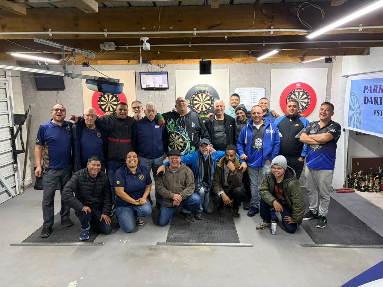 Club members and visiting players gathered at the Parklands Dart Club venue, with dartboards, the club banner and a trophy table behind them